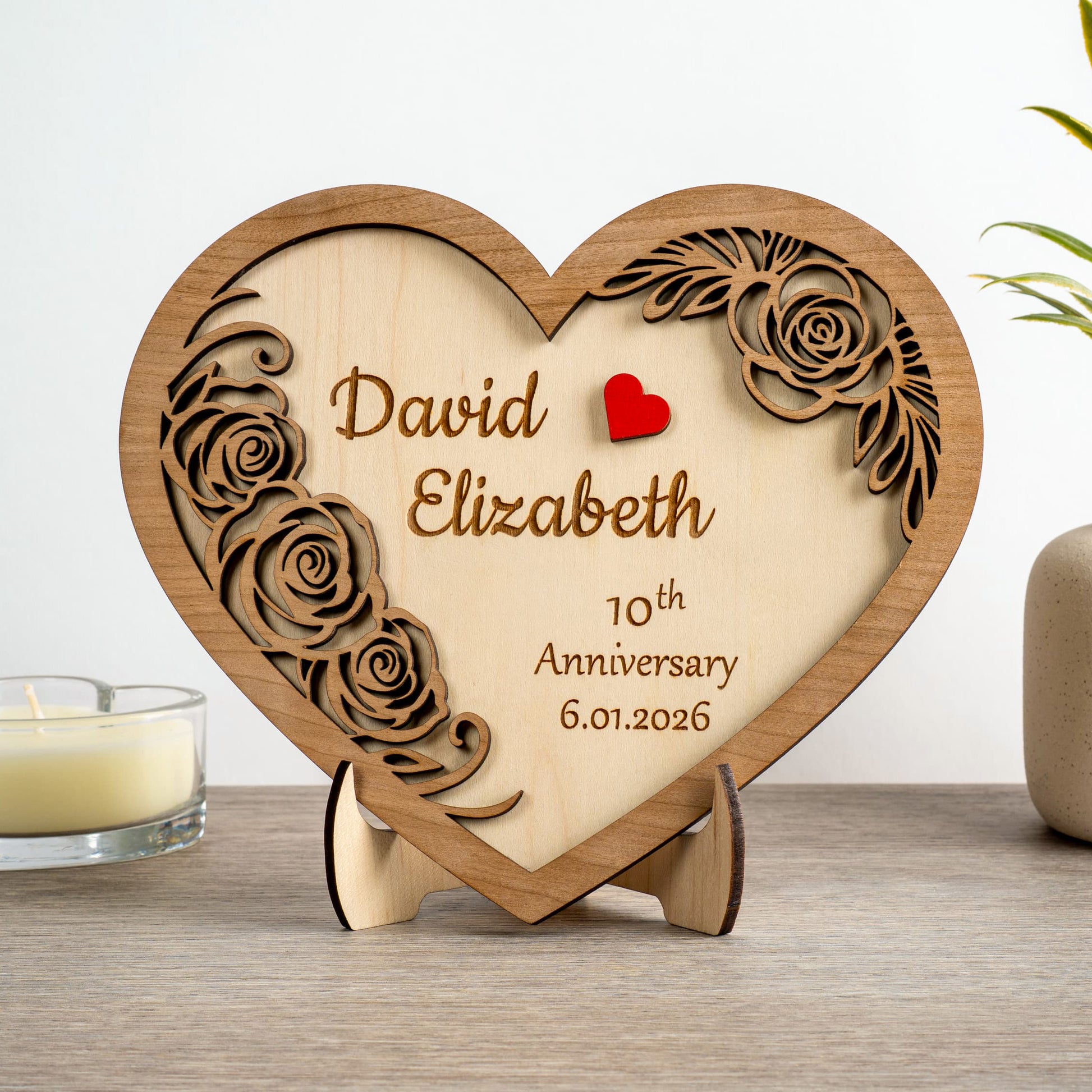 Personalised wooden heart plaque engraved with names for 10th anniversary, featuring floral design and red heart.