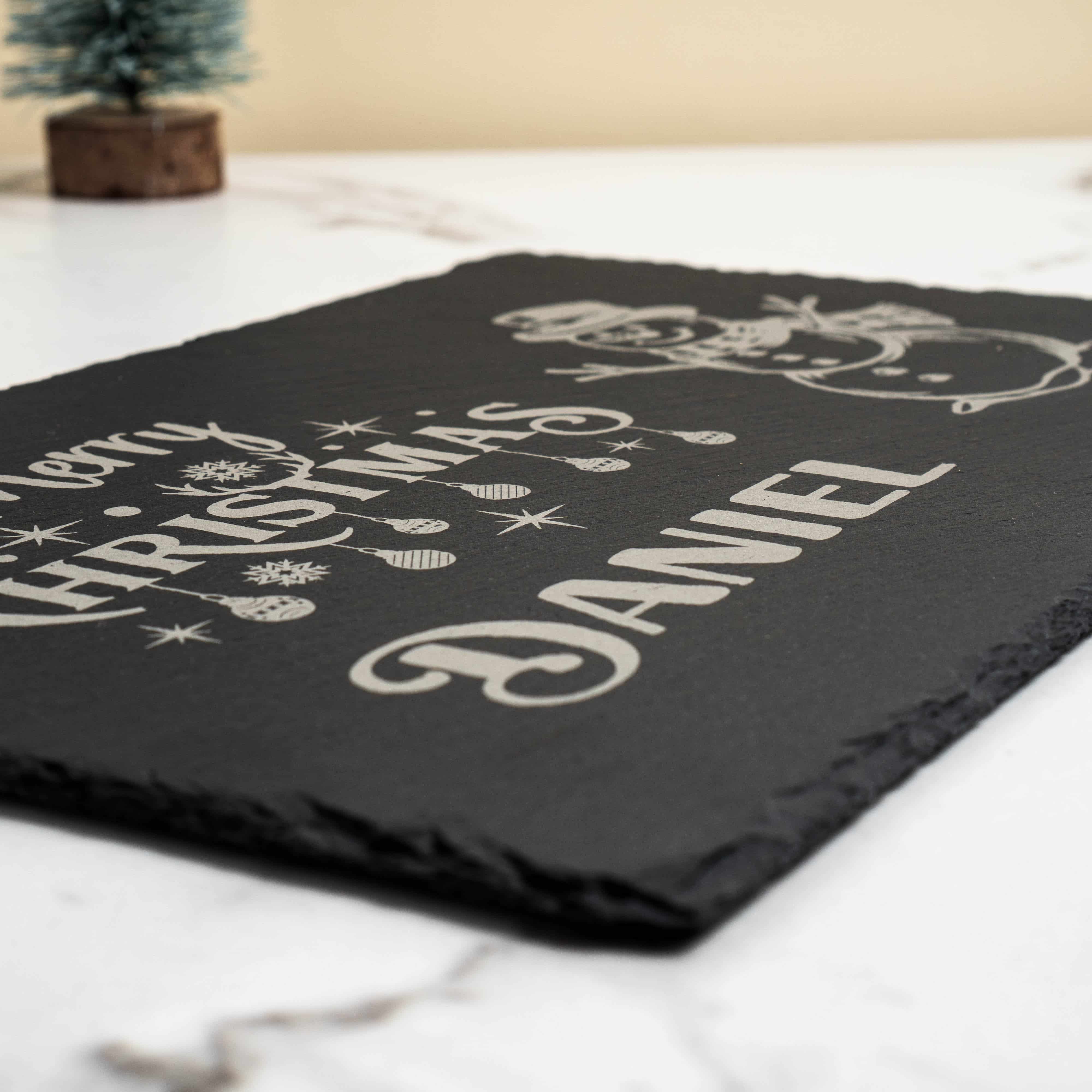 Slate table mat with 'Merry Christmas Daniel' text on a white marble table