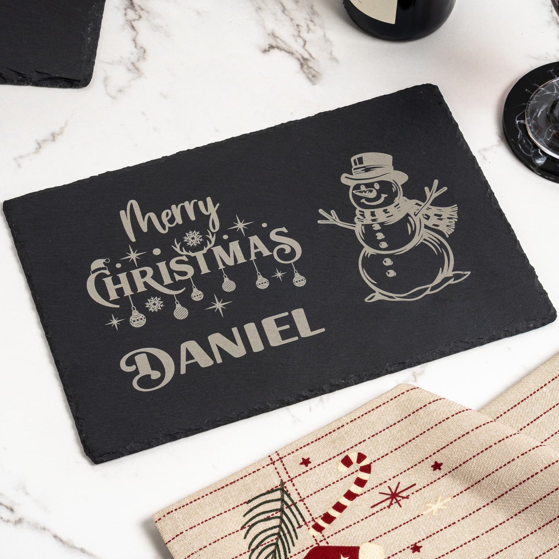 Personalised Christmas slate placemat used as festive table décor, engraved with 'Daniel', and set for a Christmas dinner with wine.