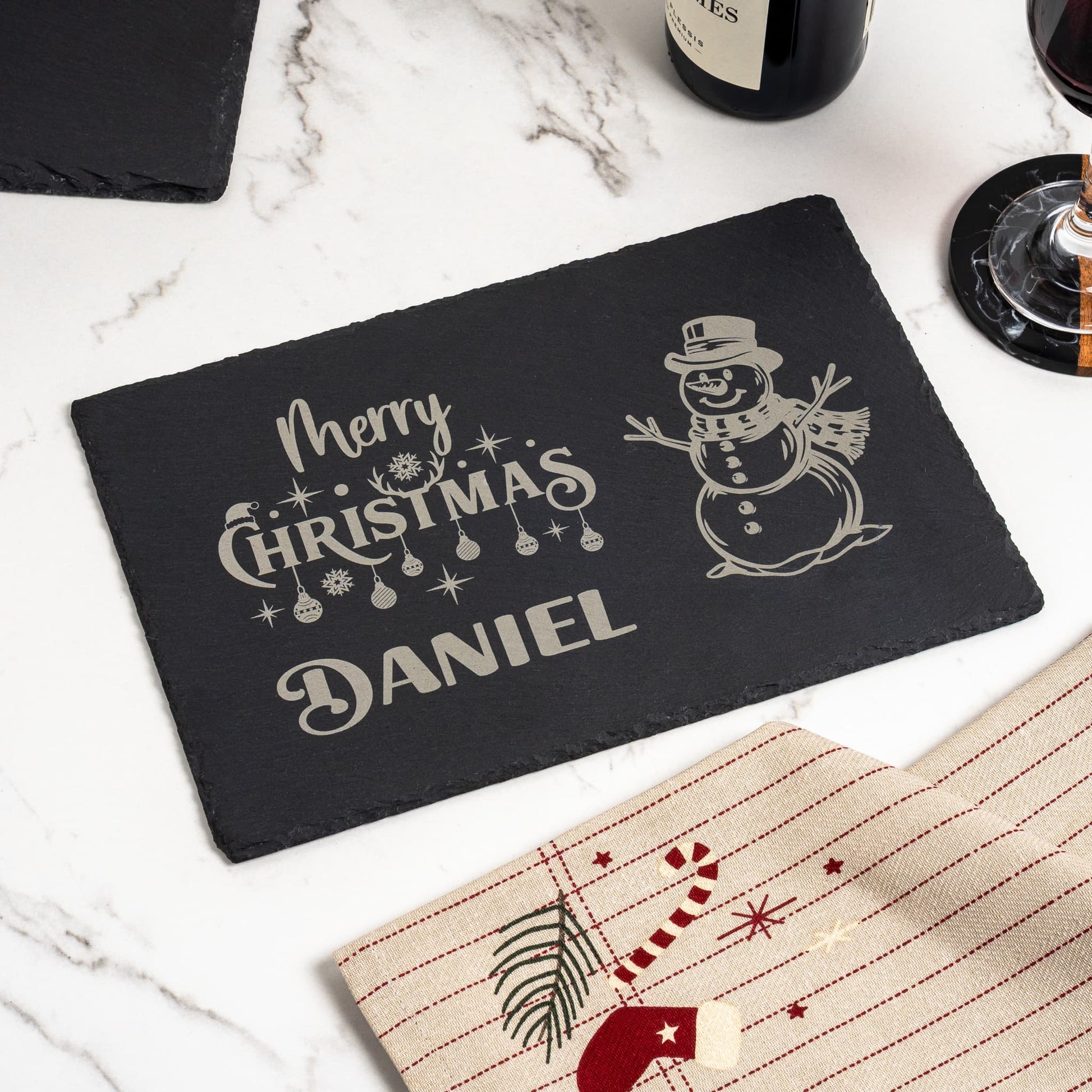 Personalised Christmas slate placemat used as festive table décor, engraved with 'Daniel', and set for a Christmas dinner with wine.