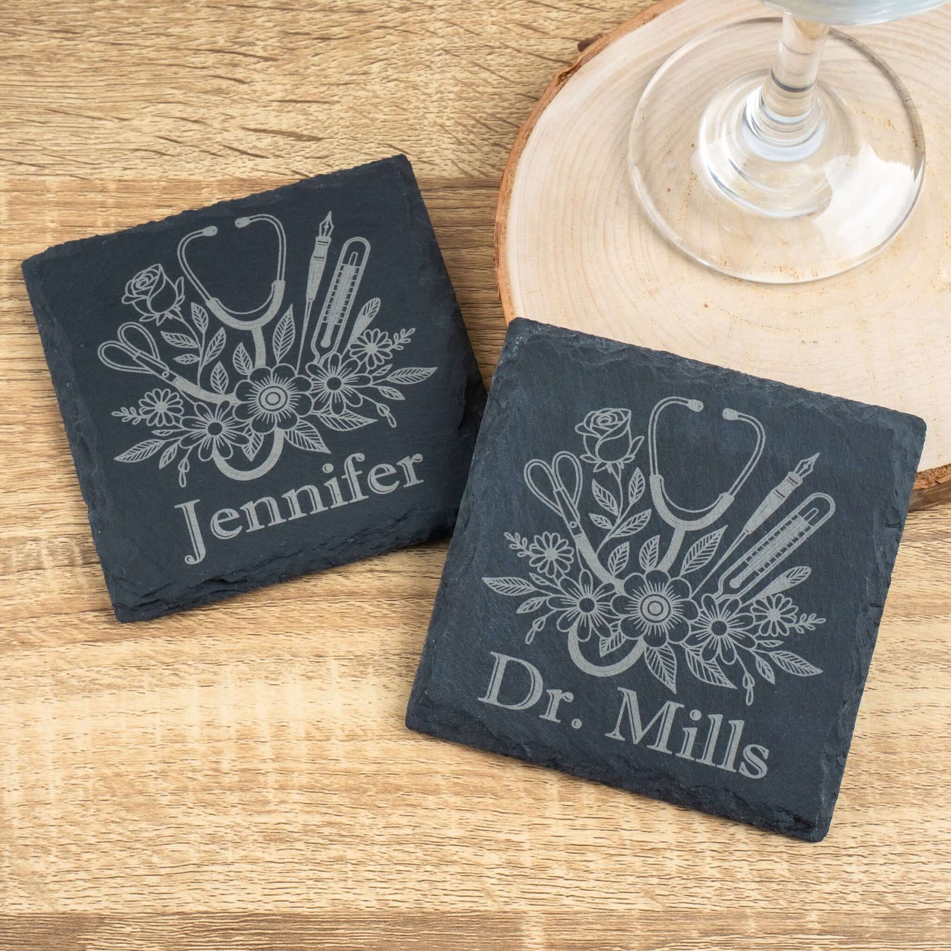 Two slate coasters with medical-themed designs and personalized names on a wooden surface.