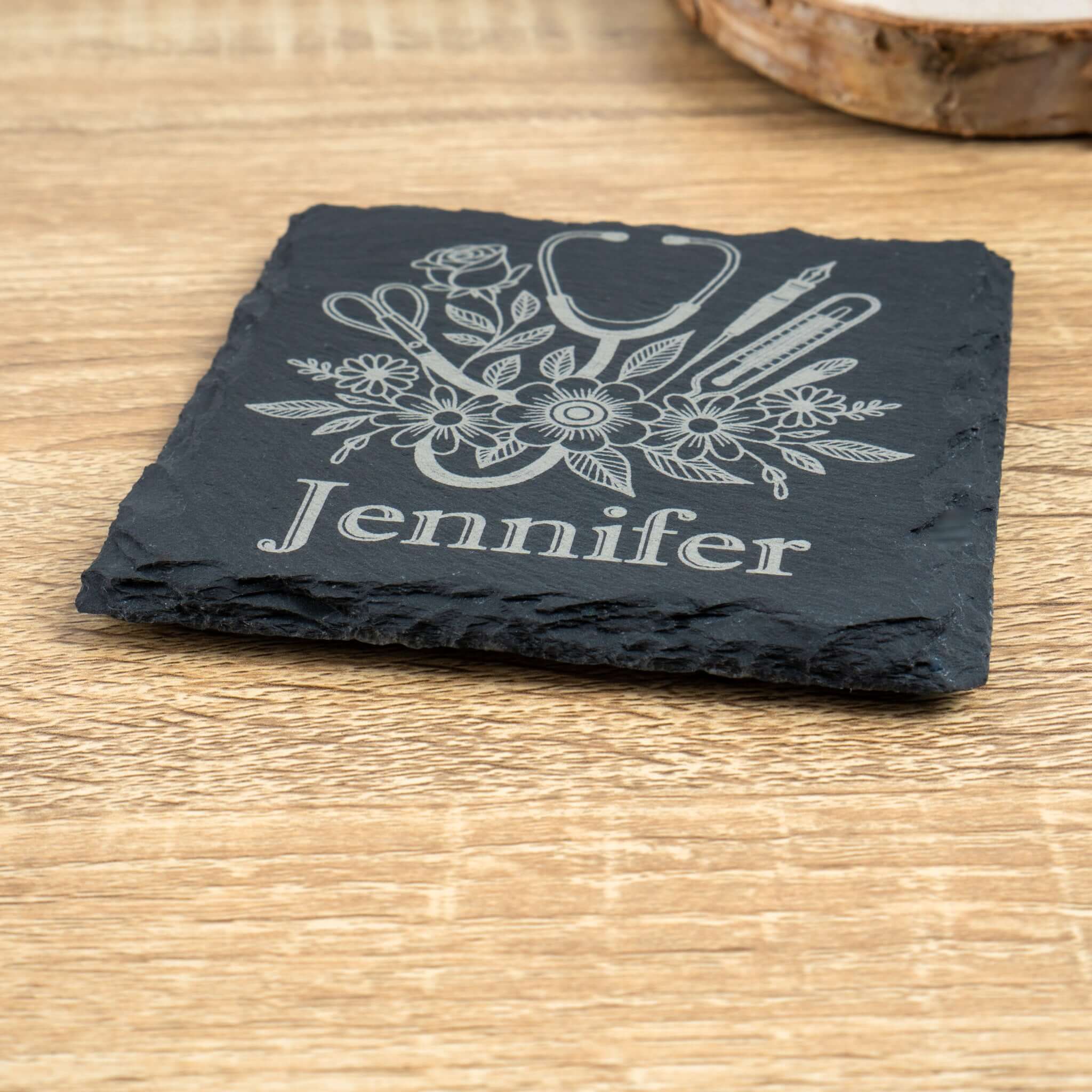 Slate coaster with engraved design and 'Jennifer' text on a wooden surface