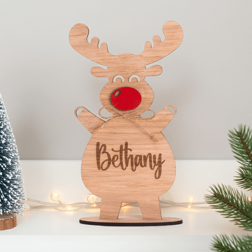 Wooden reindeer decoration with 'Bethany' engraved, surrounded by Christmas decor on a white surface.