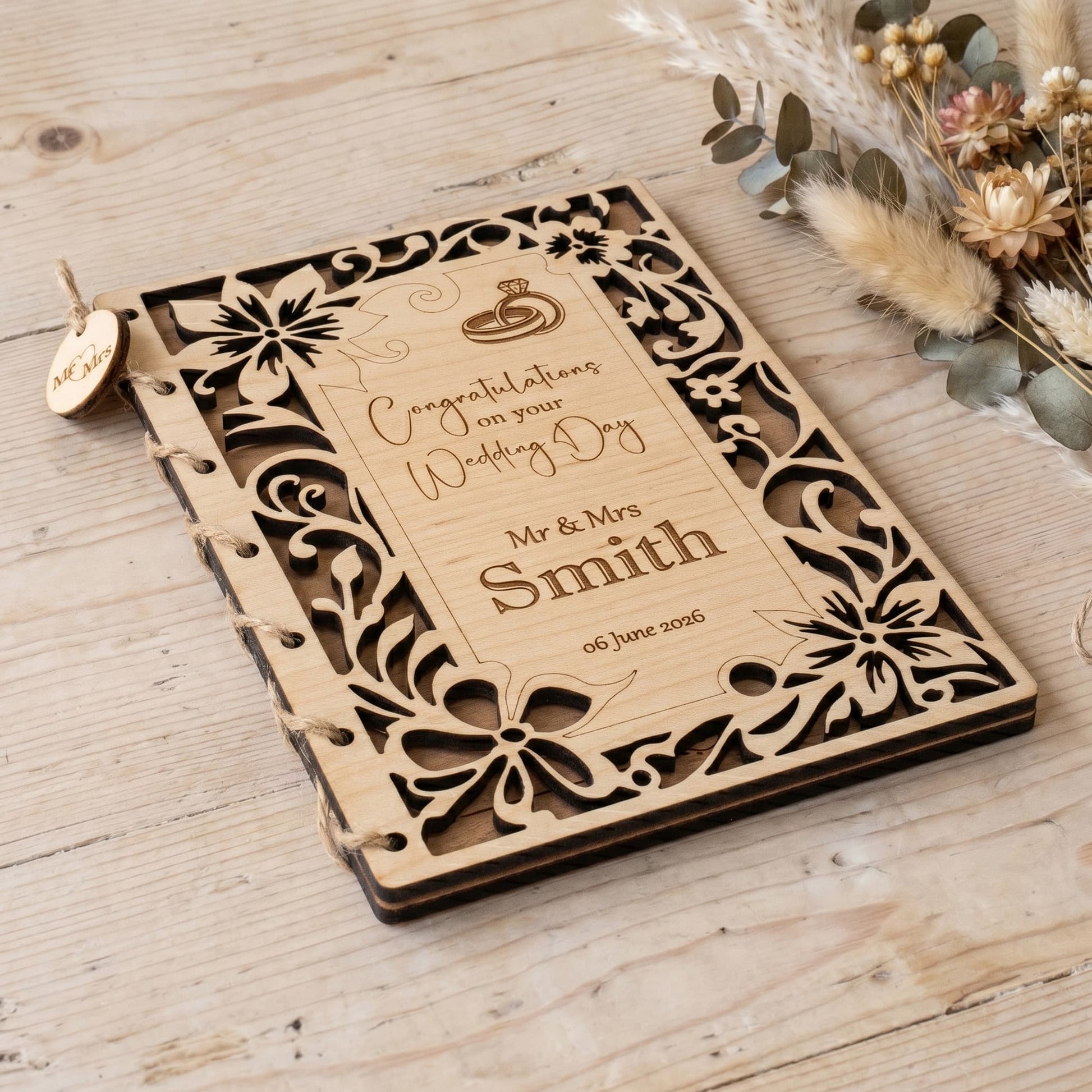 Wooden wedding card with laser-cut design on a wooden surface with dried flowers.