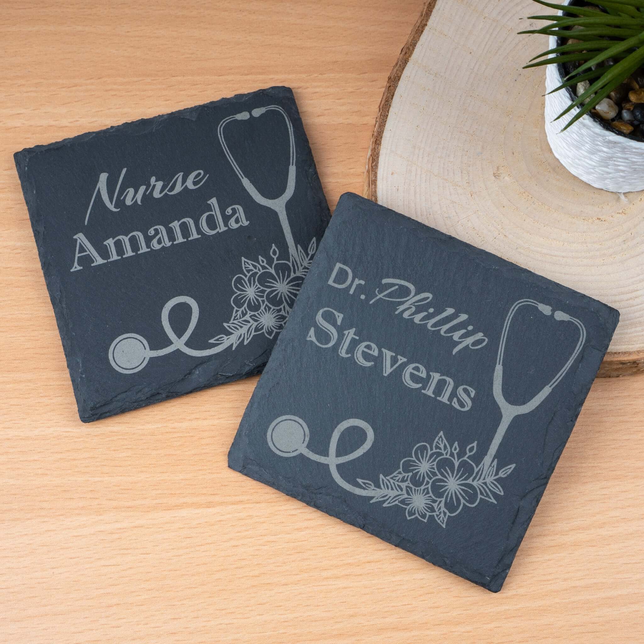 Two personalized slate coasters with stethoscope designs and engraved names on a wooden surface.
