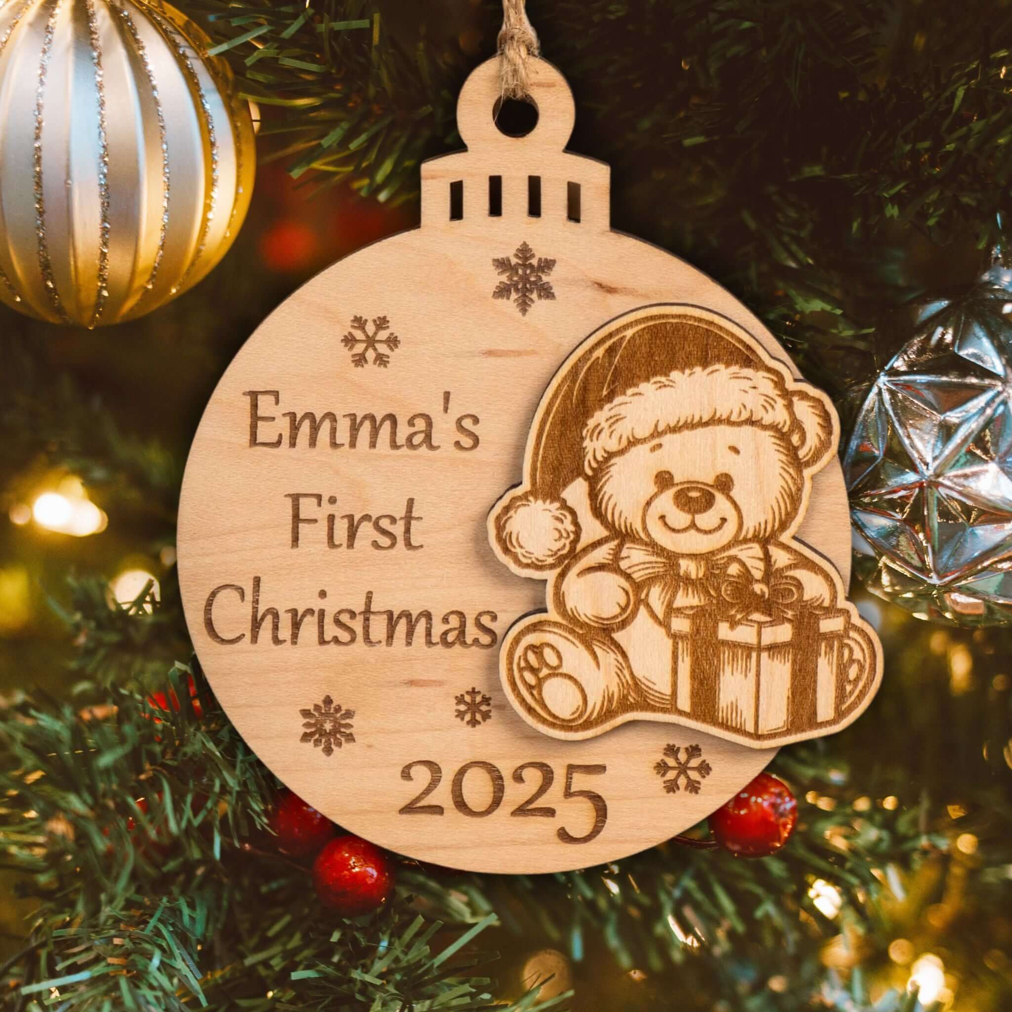 Personalised wooden first Christmas bauble with "Emma's First Christmas 2025" and teddy bear engraving, hanging on a tree.