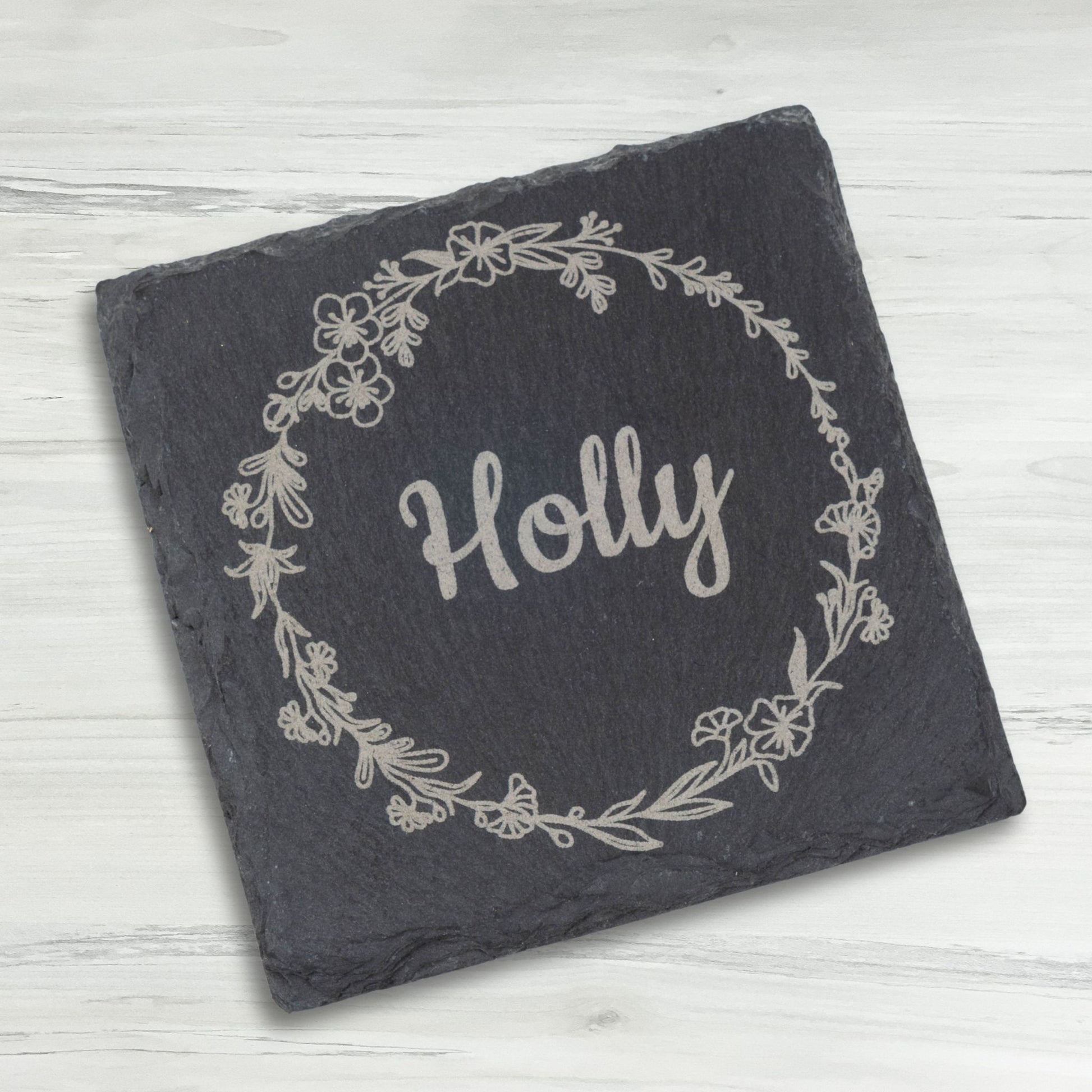 Slate coaster with 'Holly' and floral design on a light wooden surface