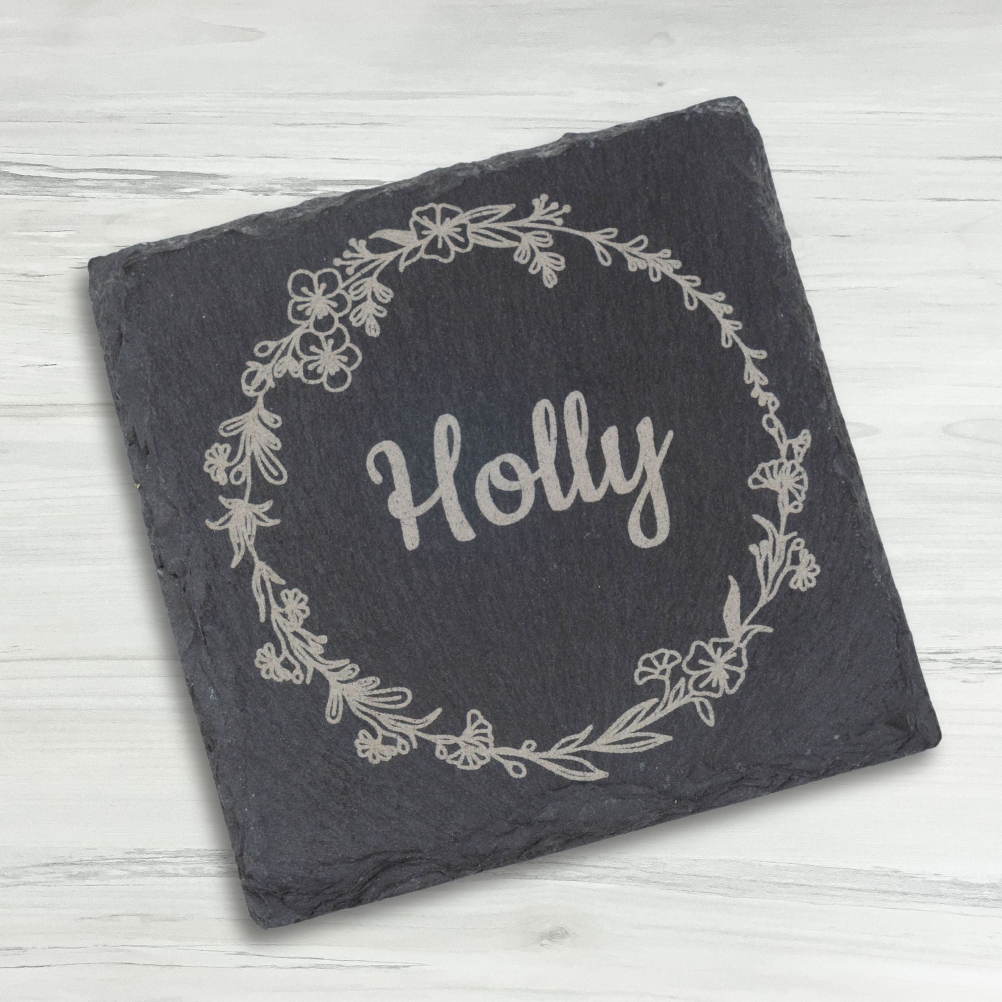 Slate coaster with 'Holly' and floral design on a light wooden surface